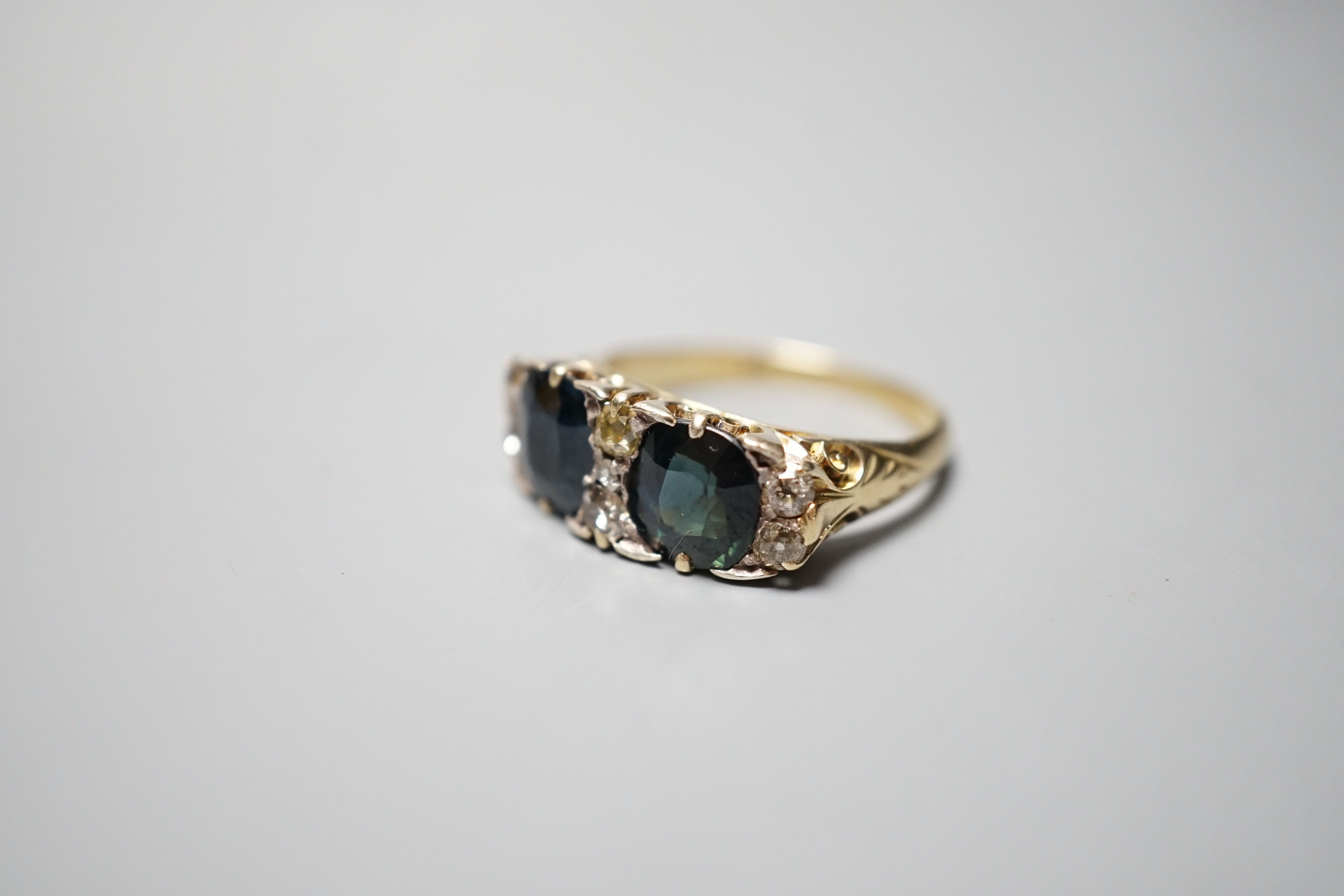 A yellow metal and two stone oval cut blue/green sapphire and seven stone diamond chip set half hoop dress ring, size Q, gross weight 5.7 grams